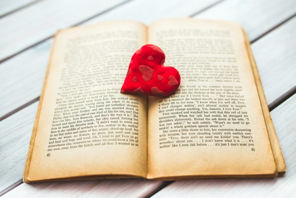 A red heart rests in an open vintage book, evoking romance.