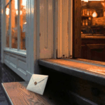 Small-town bakery at dusk with a mysterious envelope on the step — inheritance and tension imagery