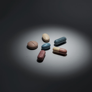 five pills of various shapes and colors resting on a reflective grey counter, a soft spotlight on the pills