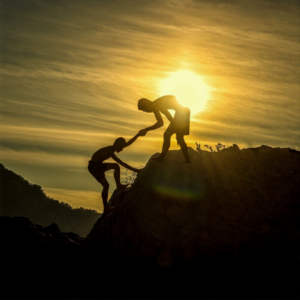 silhouettes mountain climber helping up another person