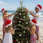 Family decorating a Christmas tree on a sunny beach, wearing Santa hats and festive outfits by the ocean.